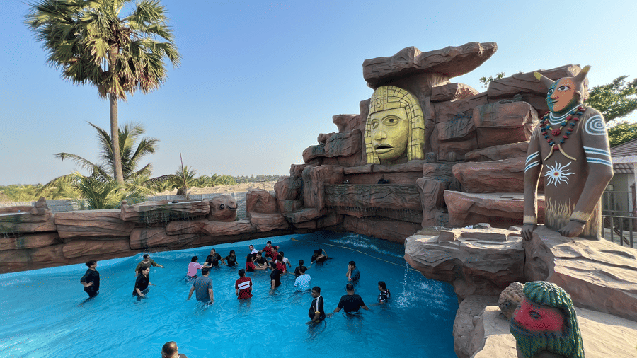 Guests swimming in a pool featuring a large decorative rock wall and tribal face sculpture - DAN Resorts & Weddings, Palghar