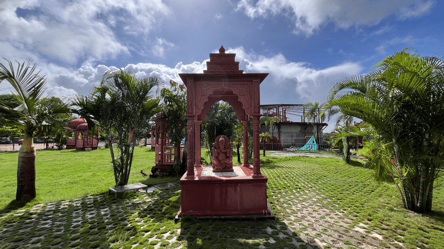 A decorative red stone shrine or gazebo centrepiece situated on a lush green lawn - DAN Resorts & Weddings, Palghar