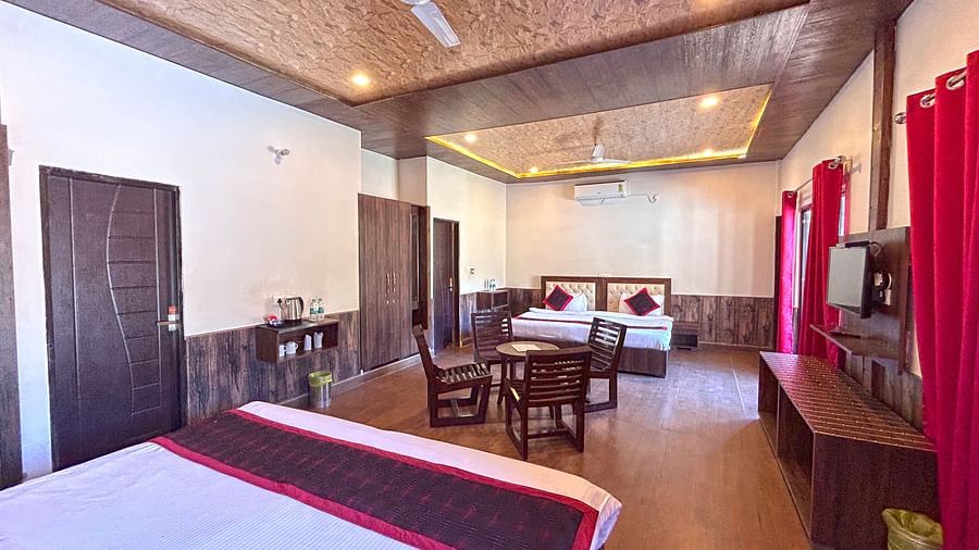 A Family Cottage with beds facing towards each other seperated by a round dining table and TV at DLS MJ River Resort, Rishikesh.