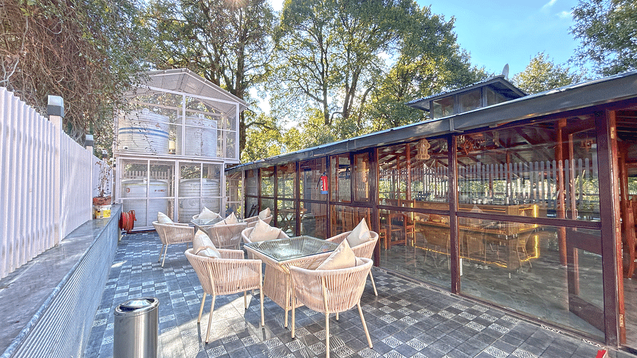 The exterior image of the restaurant featuring chairs and tables with the background of a clear sky and trees - DLS The Emerald, Nainital