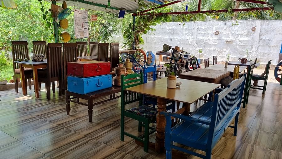 An open air dining area with wooden tables and chairs covered with a tin shed and a lush green garden in the background at Dream Vision Guest House.