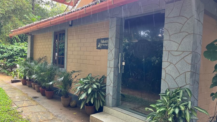 Exterior view of Robusta Meeting Hall at Evergreen County, Coorg surrounded by lush tropical plants and rustic architecture