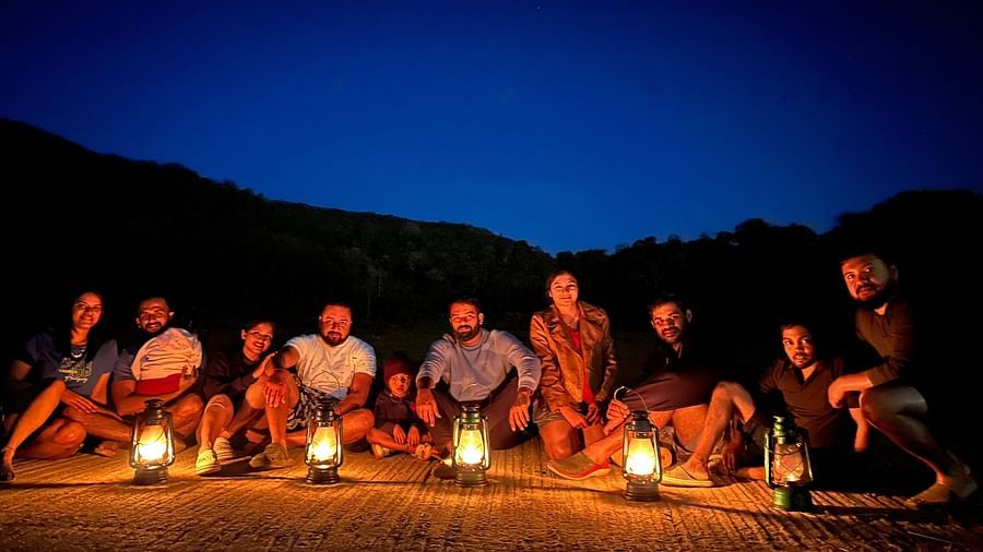 A group sitting in the dark with lanterns in front of them with a blue sky in the background - Evergreen County