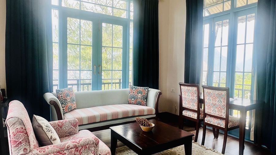 Hotel sitting area with floral chairs, wooden table, and large windows | Faraway Cottages, Auli