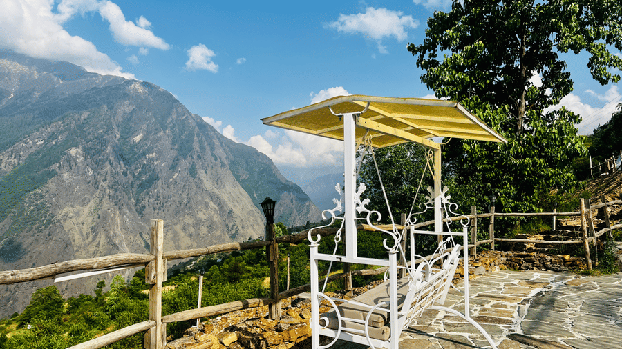 Outdoor seating area at Faraway Cottages, Auli, with white metal chairs and table on stone patio overlooking mountains.