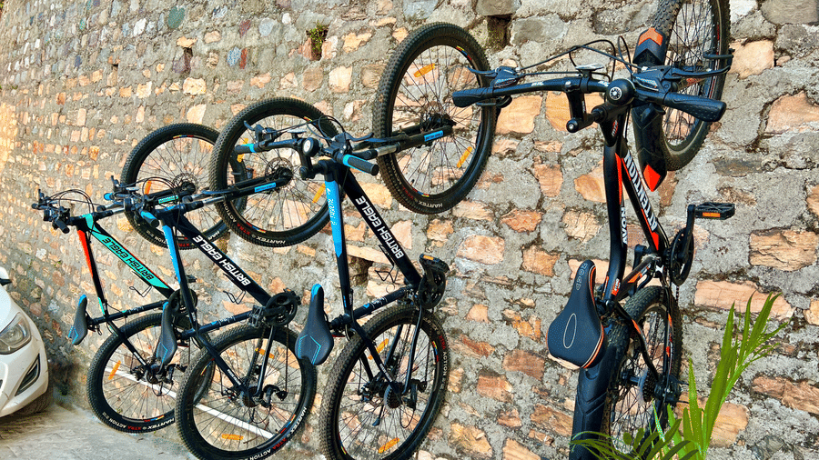 Several mountain bikes mounted vertically on an outdoor stone wall for guest use at Himalayas Resort By The Lake Hill, Mukteshwar.