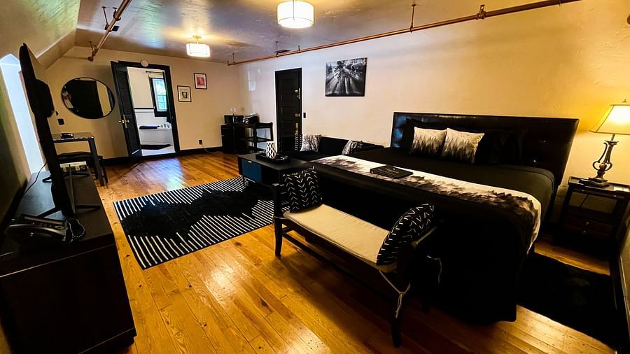 corner view of a room featuring a double bed along with a common seating are in the far end highlighting the black furnishings and decor - Historic Tapoco Lodge