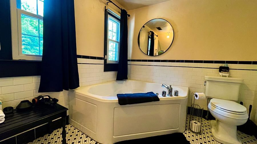 a modern bathroom featuring a bathtub along with a commode beside it and black curtains and doormat - Historic Tapoco Lodge