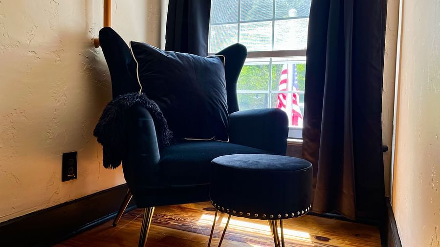 a close up shot of a clack colored cushioned armchair with a leg rest placed besidea a window with curtains - Historic Tapoco Lodge
