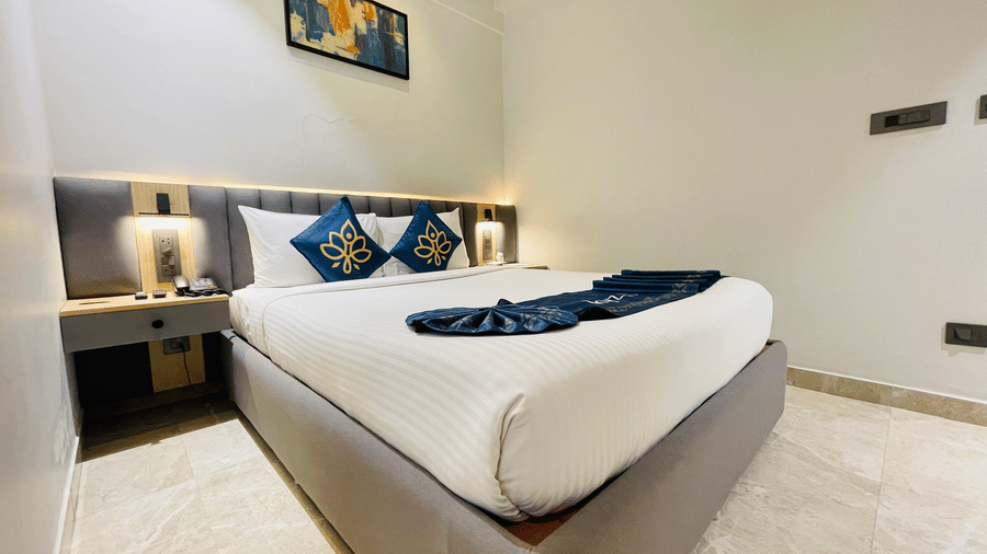 An angled view of a king bed with white bedding and blue accent pillows at Hotel Kyzen HiTech City with a grey upholstered headboard framed artwork and warm bedside lighting.
