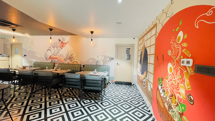 A lounge dining area at Hotel Kyzen HiTech City featuring grey sofas patterned black and white flooring a bold red wall with colorful mural artwork and warm ambient lighting.