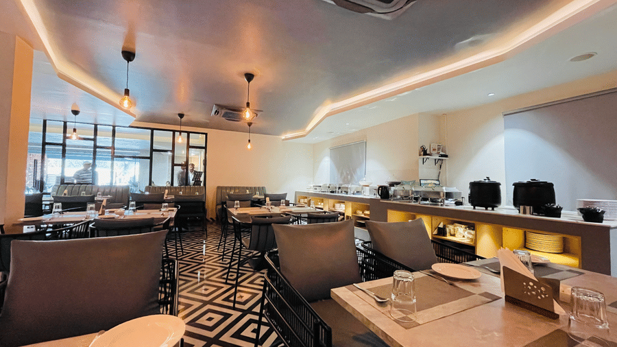 A restaurant seating area at Hotel Kyzen HiTech City featuring grey upholstered chairs marble topped tables patterned black and white flooring and warm pendant lighting.