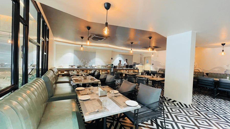 A wide angle view of the restaurant at Hotel Kyzen HiTech City featuring booth seating grey chairs marble tables patterned flooring large windows and warm pendant lighting.