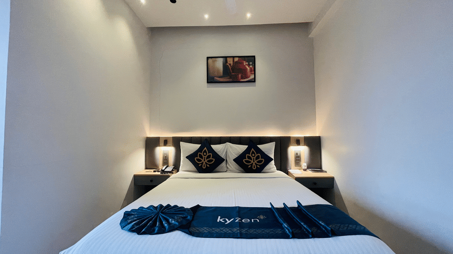 An overhead view of a king bed with white bedding blue accent pillows and decorative towel folding at Hotel Kyzen HiTech City with a grey headboard and warm recessed ceiling lighting.
