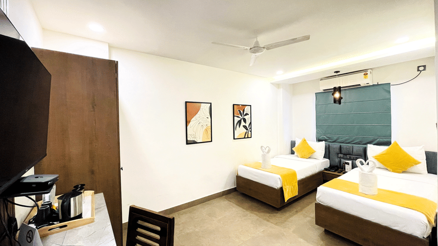 Twin bed room at Hotel Kyzen Smart Stays Madhapur with yellow accent bedding, teal headboard wall panel, wooden wardrobe, work desk, and warm ceiling lighting.