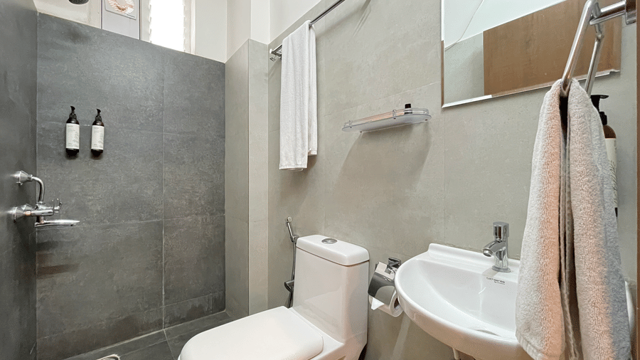 Modern bathroom at Hotel Kyzen Smart Stays Madhapur featuring an open shower area, toilet, wash basin, grey tiled walls, and neatly placed toiletry bottles.