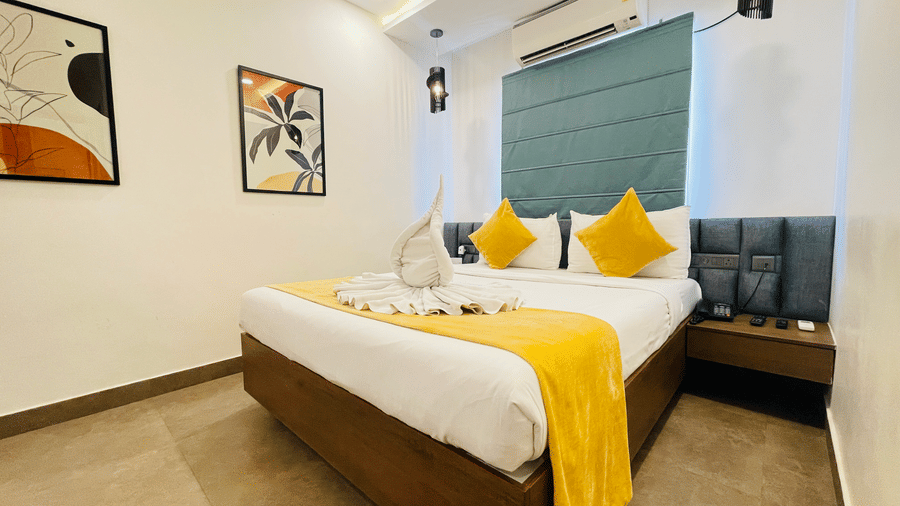 Double bed room at Hotel Kyzen Smart Stays Madhapur featuring a king bed with yellow and white bedding, teal headboard panel, framed artwork, and warm ceiling lighting.