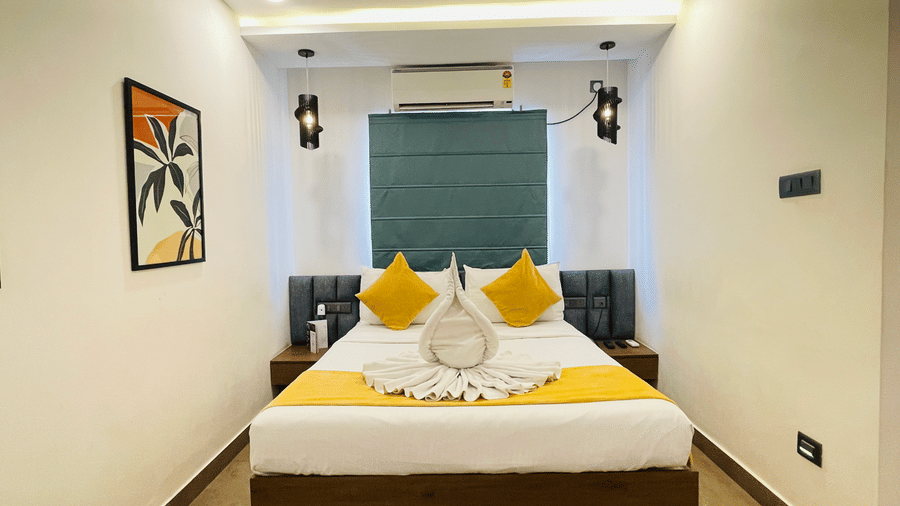 King bed room at Hotel Kyzen Smart Stays Madhapur with yellow and white bedding, swan towel folding, teal headboard panel, wall sconces, and framed artwork above the bed.