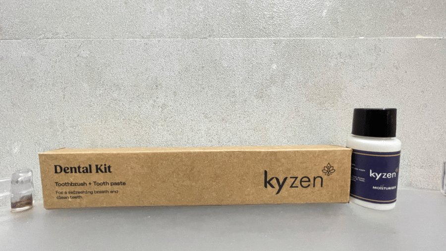 Close-up of Kyzen branded dental kit with toothbrush, toothpaste box, and a toiletry bottle placed on a white surface at Hotel Kyzen Smart Stays Madhapur.
