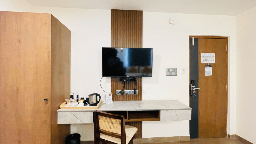 Hotel room at Hotel Kyzen Smart Stays Madhapur with wall-mounted TV, work desk, wooden wardrobe, room door, and clean white walls with warm lighting.
