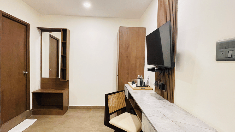 Hotel room entrance view at Hotel Kyzen Smart Stays Madhapur featuring a wall-mounted TV, work desk, wooden wardrobe, room door, and clean white walls.