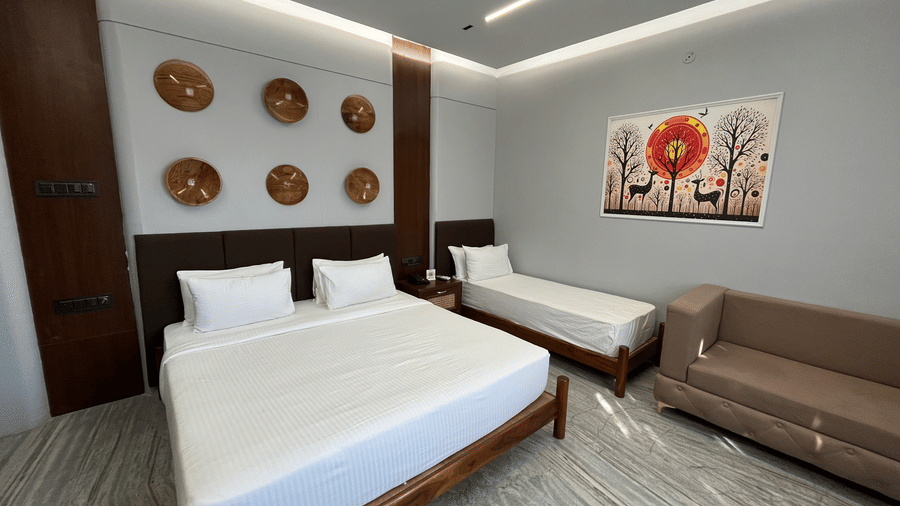 Front view of the bedding at the Suite of Hotel Mumbai House, Pithampur, with a brown 2-seater couch placed in front of it.