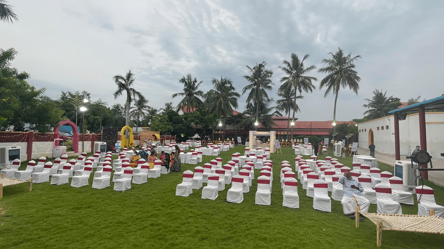A wide view of the spacious outdoor lawn venue featuring lush green grass and towering palm trees under a clear sky - Kailash Conventions ECR