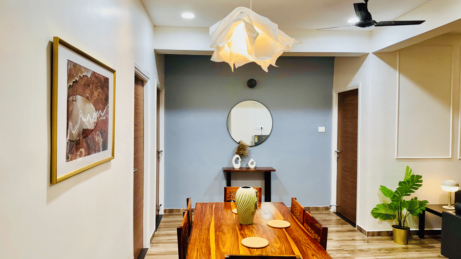 Dining area and common space in the Coral 4BHK at Kove Smart Stays featuring its wooden dining table and chairs placed at the centre of a common space that leads to doorways, and walls that are adorned with paintings and set-ups.
