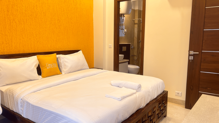 Bedroom of Lime Tree Hotels & Service Apartment Private Limited featuring a carved wooden bed frame and an orange accent wall.