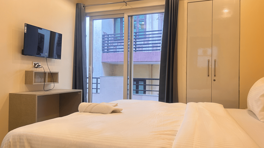 Bedroom of Lime Tree Hotels & Service Apartment Private Limited featuring a wall mounted television and a balcony with glass doors.