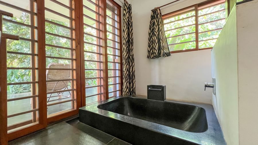 Villa Washroom with black tiled bath tub and comes with a outside nature view of the surroundings.