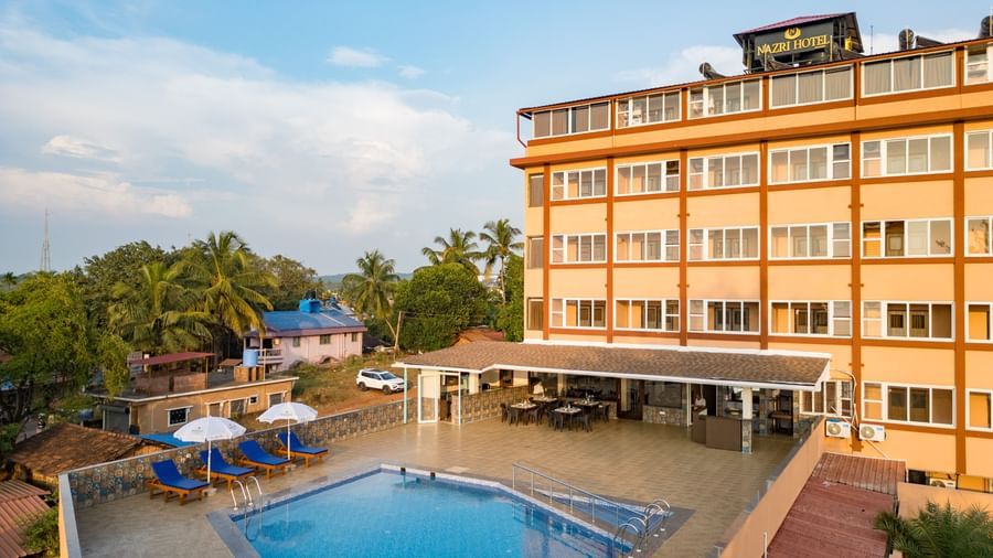 A serene view of the outdoor swimming pool surrounded by sun loungers and palm trees at Nazri The Verda, Arambol.