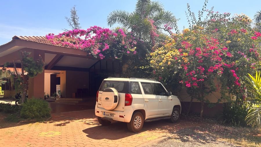 A car parked under a carport at Paradise Wild Hills Resort, Kollur, surrounded by colourful flowering plants.