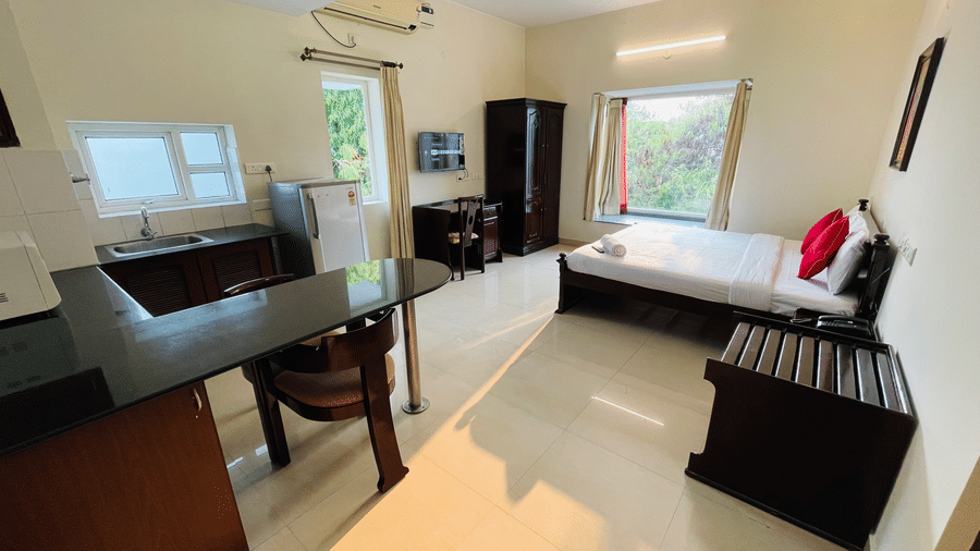 Hotel room with a double bed, a study table, and a window with greenery views at Sanctum Suites Indiranagar, Bangalore.