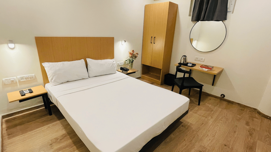 Sanctum Suites, Richmond Road, Bangalore offers a room with a double bed, a tall wooden wardrobe, a desk with a round mirror, a chair, and wood effect flooring.