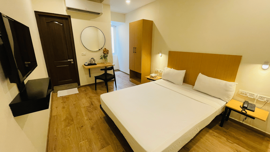 A room at Sanctum Suites, Richmond Road, Bangalore featuring a large bed, a wardrobe,a dressing table with a mirror, chair, a wall mounted television, and an A/C.