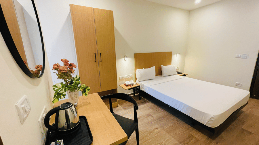 A room featuring a double bed, a side table with a kettle, and flower pot at Sanctum Suites, Richmond Road, Bangalore.