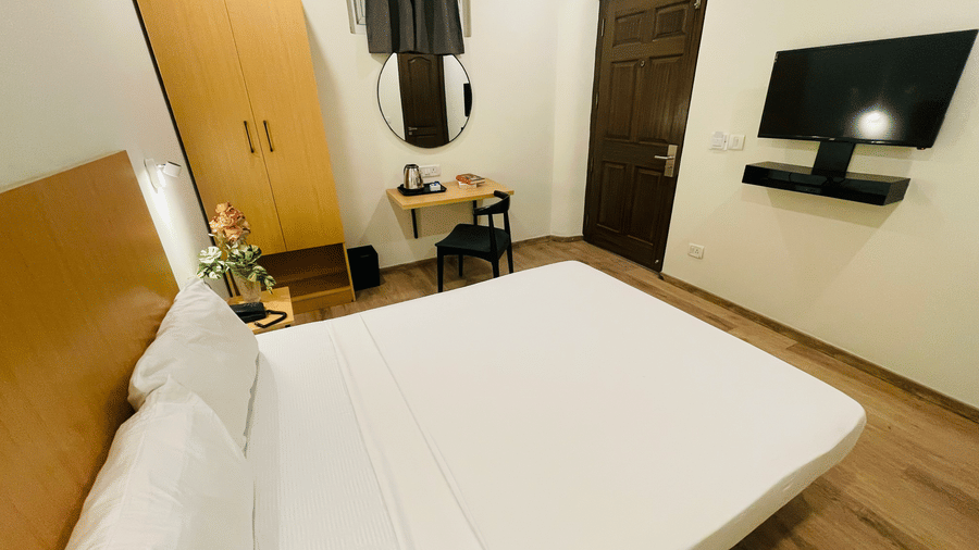 A double bedroom with a wall mounted TV, a desk, a mirror, and a cupboard at Sanctum Suites, Richmond Road, Bangalore.