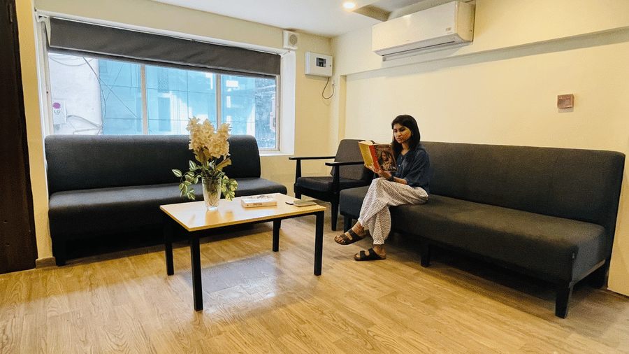 The waiting lounge at Sanctum Suites, Richmond Road, Bangalore has 2 black sofas, a wooden coffee table with flowers, and a window.