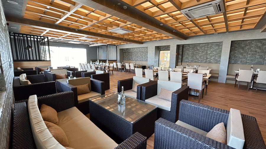 A restaurant interior with wicker sofas in a lounge area and dining tables in the background under a wooden slatted ceiling