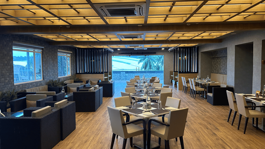 A dining area with square tables and chairs arranged on a wooden floor under a decorative ceiling