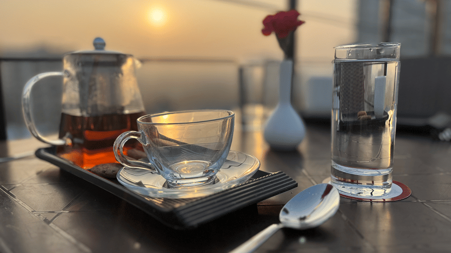 Rooftop dining setup with tea pot and a glass cup with a beautiful sunset view - Senses Hotel