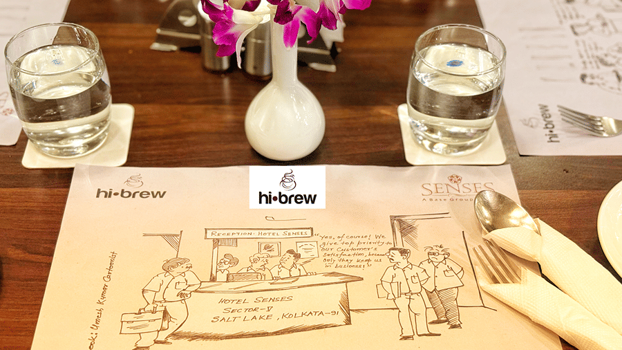 A table mat made of paper with a caricature printed on it along with a glasses of water at the Hi Brew Restaurant at Senses Hotels.