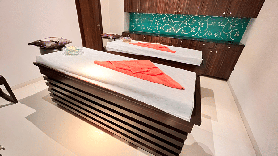 A serene spa treatment room with two neatly prepared massage tables, crisp linens, folded towels, and elegant wooden cabinetry for relaxation at Springs Hotel & Spa, Bangalore