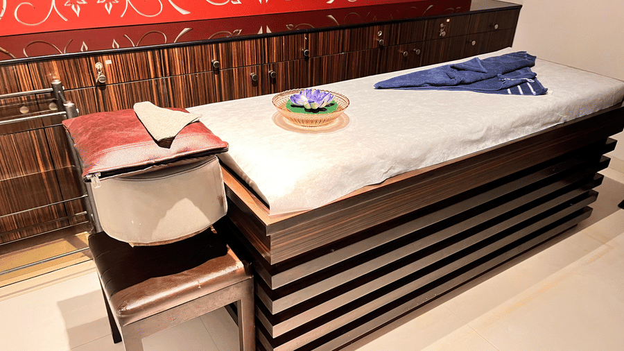 A neatly arranged spa therapy room with a cushioned massage table, folded towels, floral decor, and warm red patterned wall design at Springs Hotel & Spa, Bangalore