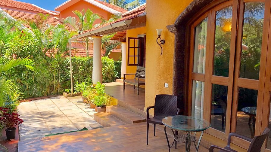 Exterior sitting area during daytime at The Bungalows Light House, Goa featuring a coffee table and a pair of chairs with lush greenery in the surroundings