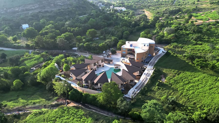 An aerial view of The Qualia Resort Club & Brewery, Udaipur surrounded by lush greenery and hills.