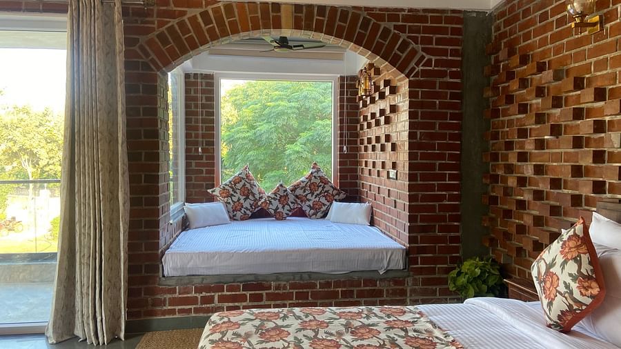 A bedroom at Tisya Farms, Gurgaon featuring a bed near a large arched window, brick walls, and a curtain on one side.
