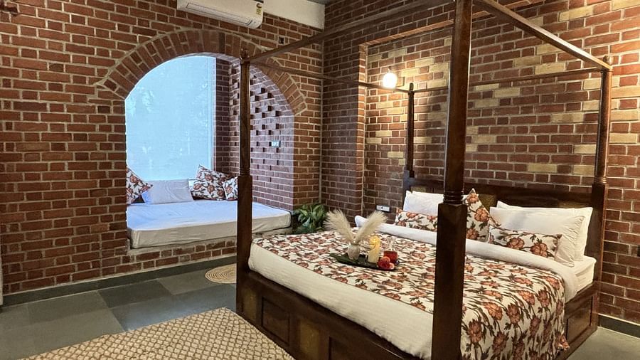 Double bed with brick wall backdrop and arched window in a cosy room at Tisya Farms, Gurgaon.