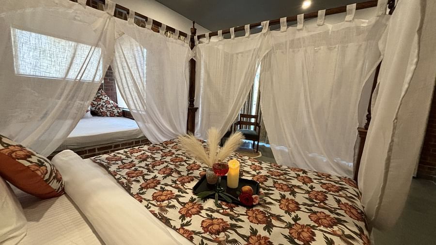 A bedroom at Tisya Farms, Gurgaon with a canopy bed, white curtains, and floral bedding with a tray of refreshments.